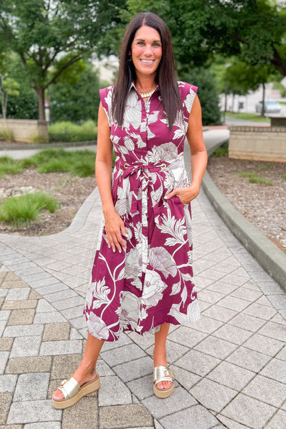 Front view of woman wearing Swagger Boutique’s floral midi dress standing outside at a park.