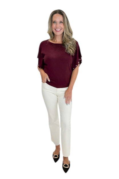 Front view of woman wearing Swagger Boutique’s Wine Grommet Sleeve Knit Top by Entro with jeans against white studio background.