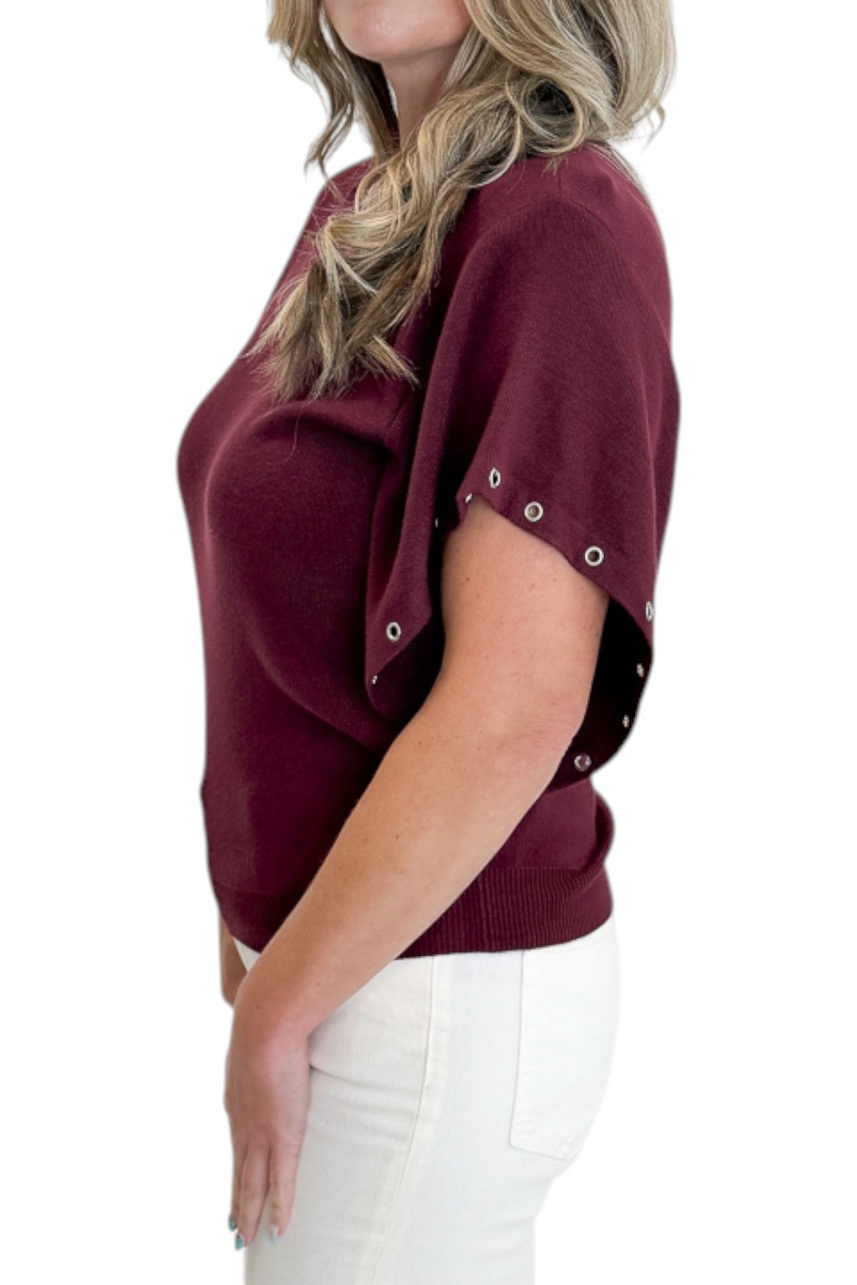 Side detail view of woman wearing Swagger Boutique’s Wine Grommet Sleeve Knit Top by Entro with jeans against white studio background.