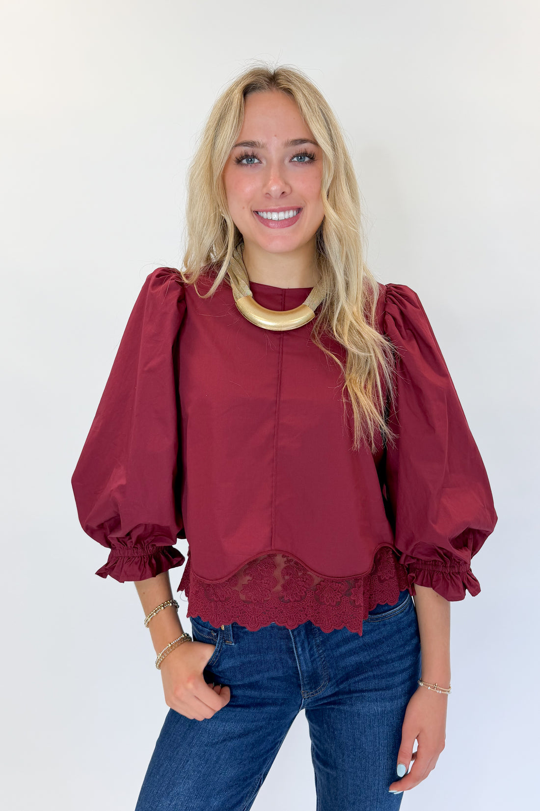 Front view of woman wearing Swagger Boutique’s Wine Lace Trim Top by Entro with jeans against white studio background.