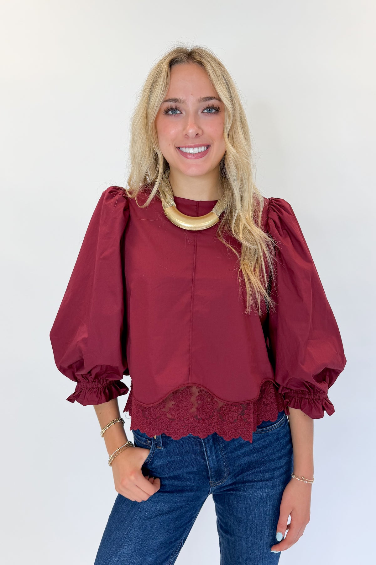 Front view of woman wearing Swagger Boutique’s Wine Lace Trim Top by Entro with jeans against white studio background.