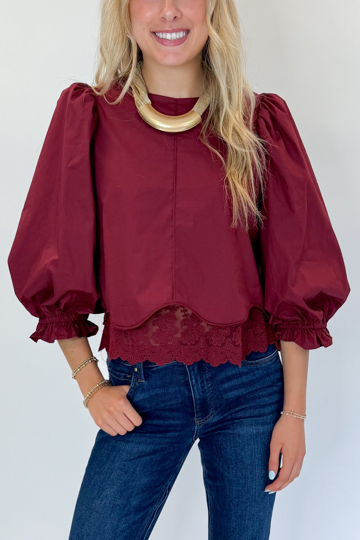 Front detail view of woman wearing Swagger Boutique’s Wine Lace Trim Top by Entro with jeans against white studio background.