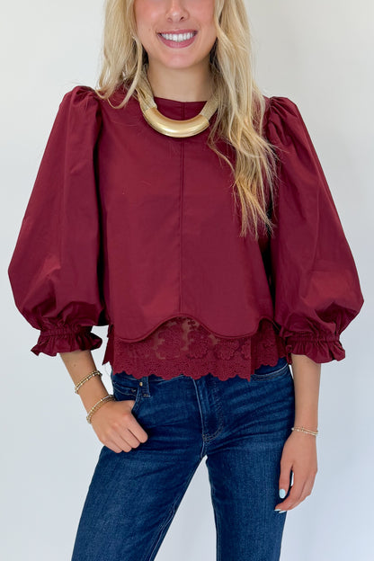 Front detail view of woman wearing Swagger Boutique’s Wine Lace Trim Top by Entro with jeans against white studio background.