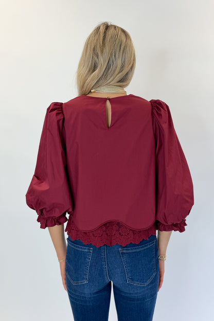 Back view of woman wearing Swagger Boutique’s Wine Lace Trim Top by Entro with jeans against white studio background.