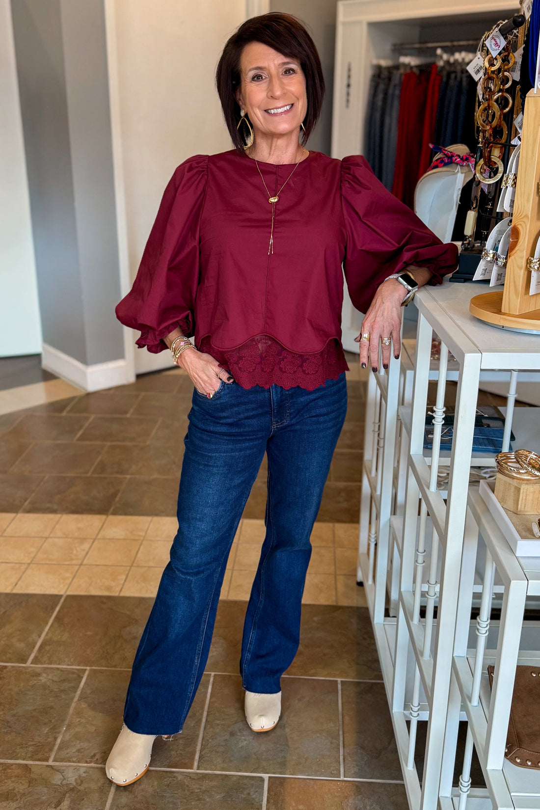 Front view of woman wearing Swagger Boutique’s Wine Lace Trim Top by Entro with jeans standing at the store.