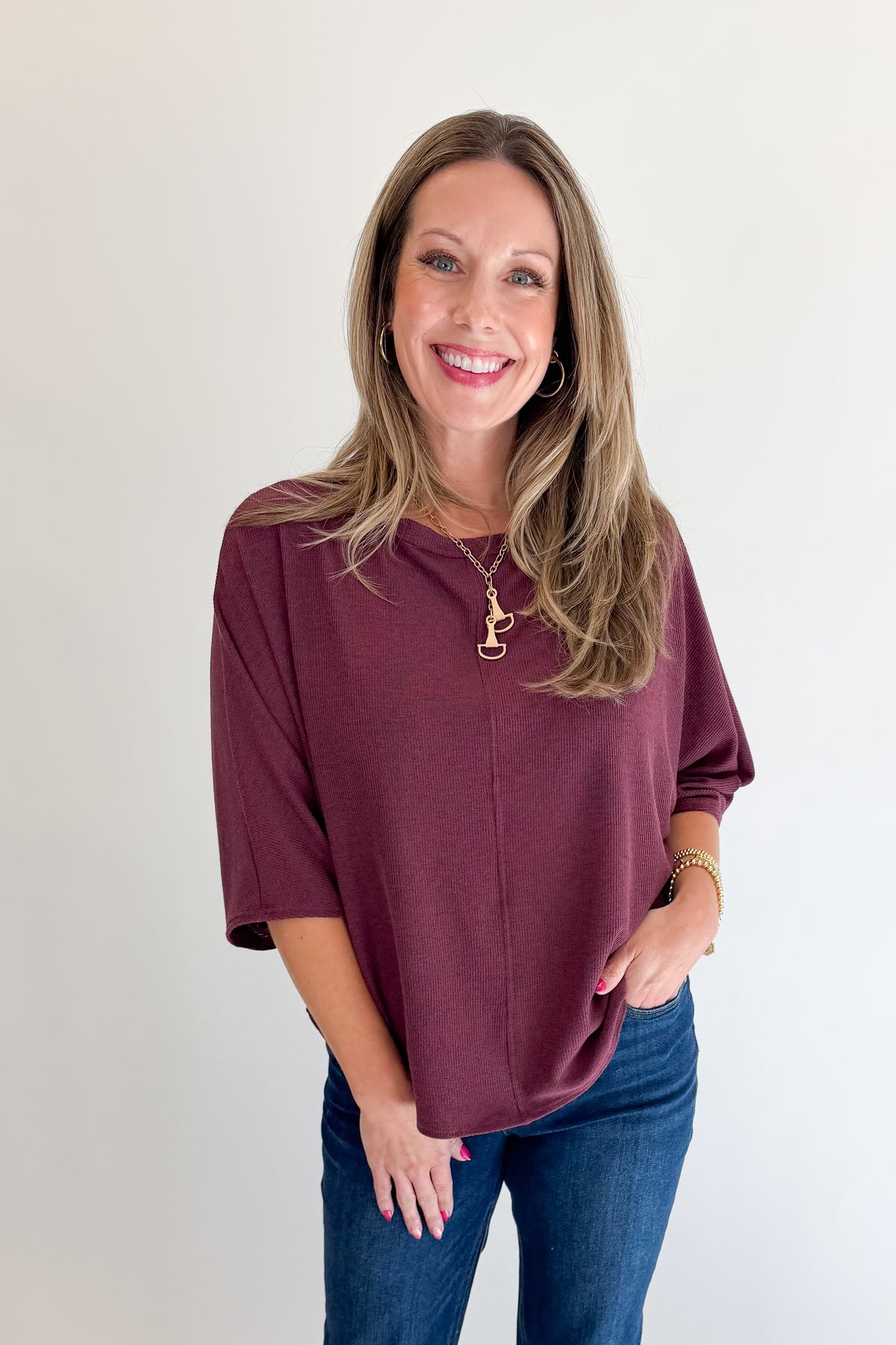 Front view of woman wearing Swagger Boutique’s Wine Ribbed Dolman Sleeve Top with jeans against white studio background.