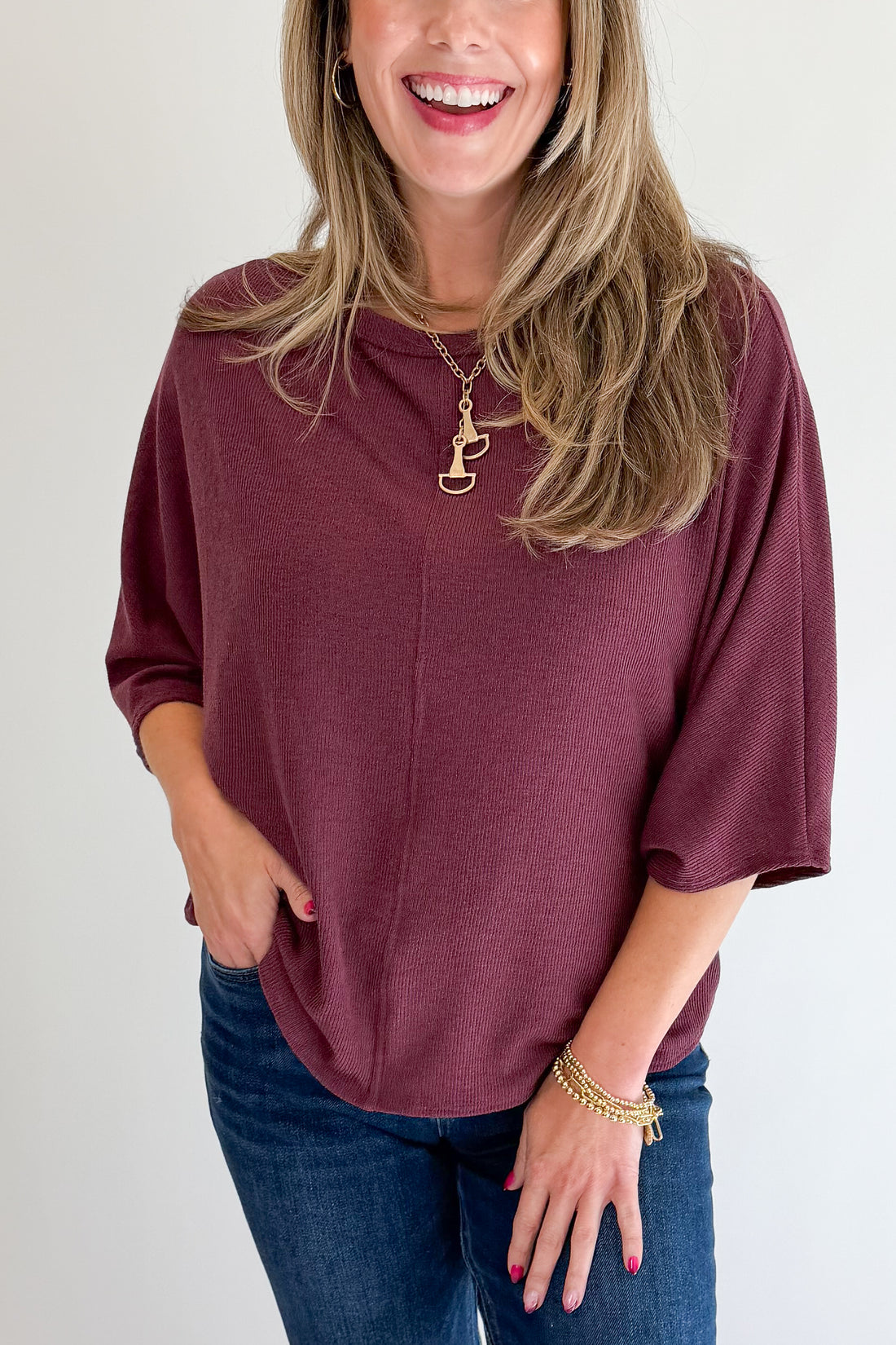 Front detail view of woman wearing Swagger Boutique’s Wine Ribbed Dolman Sleeve Top with jeans against white studio background.