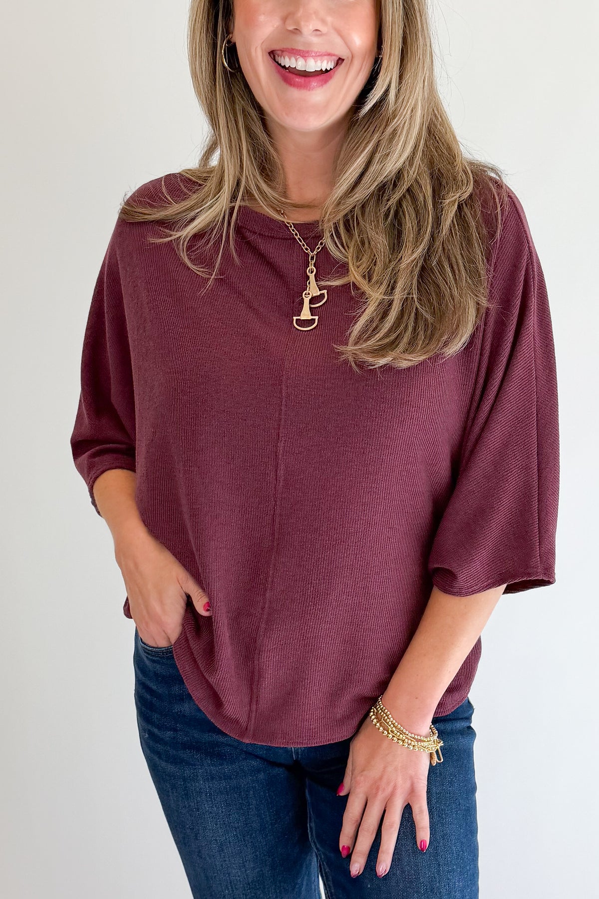Front detail view of woman wearing Swagger Boutique’s Wine Ribbed Dolman Sleeve Top with jeans against white studio background.