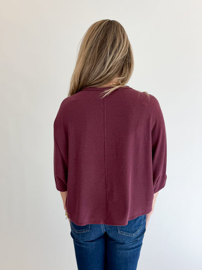 Back view of woman wearing Swagger Boutique’s Wine Ribbed Dolman Sleeve Top with jeans against white studio background.