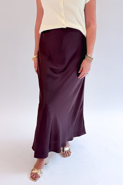 Front detail view of woman wearing Swagger Boutique’s Wine Satin Maxi Skirt with sweater against white studio background.