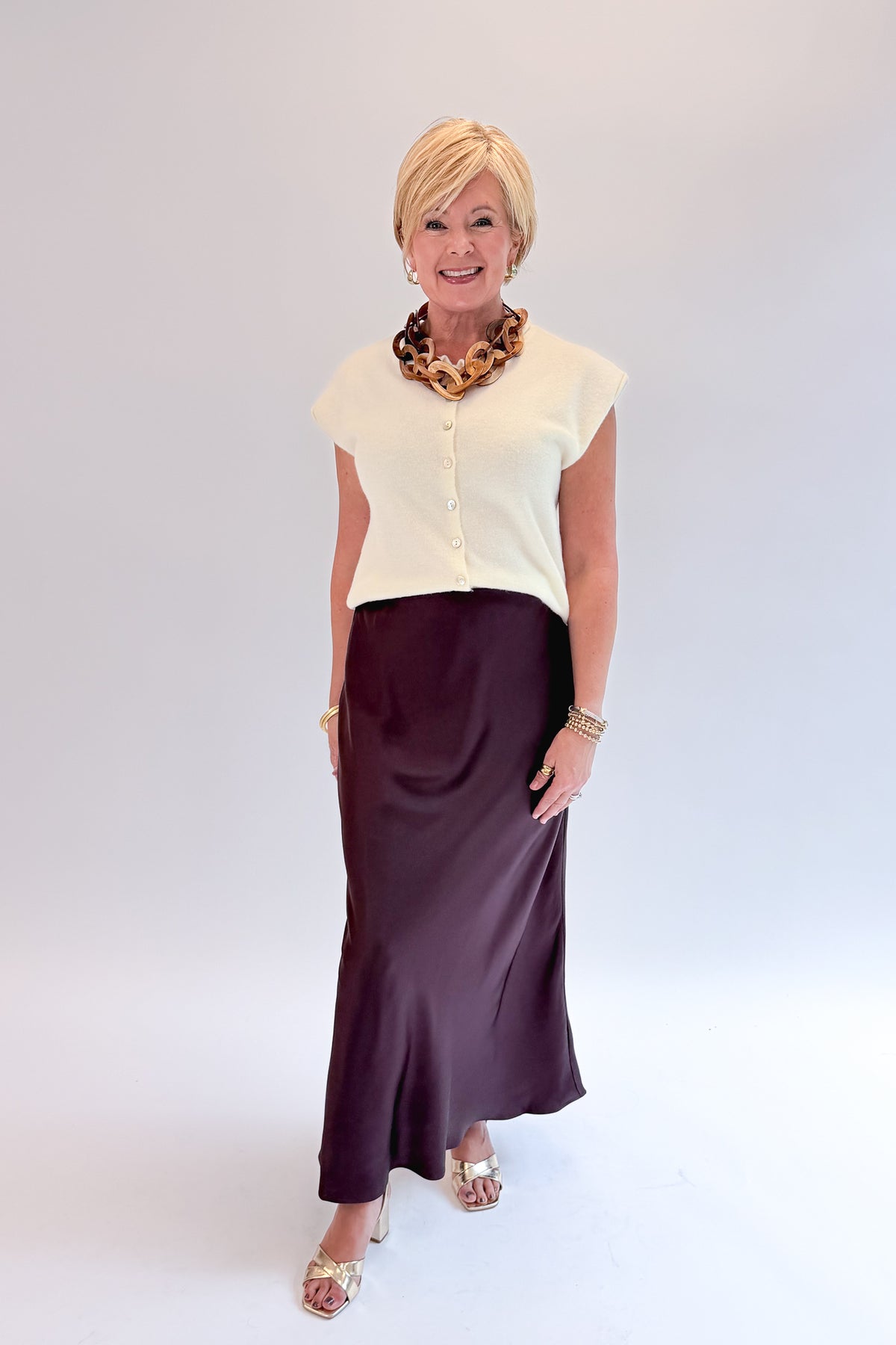 Front view of woman wearing Swagger Boutique’s Wine Satin Maxi Skirt with sweater against white studio background.