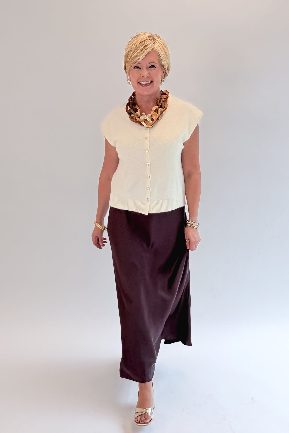 Front view of woman wearing Swagger Boutique’s Wine Satin Maxi Skirt with sweater against white studio background.
