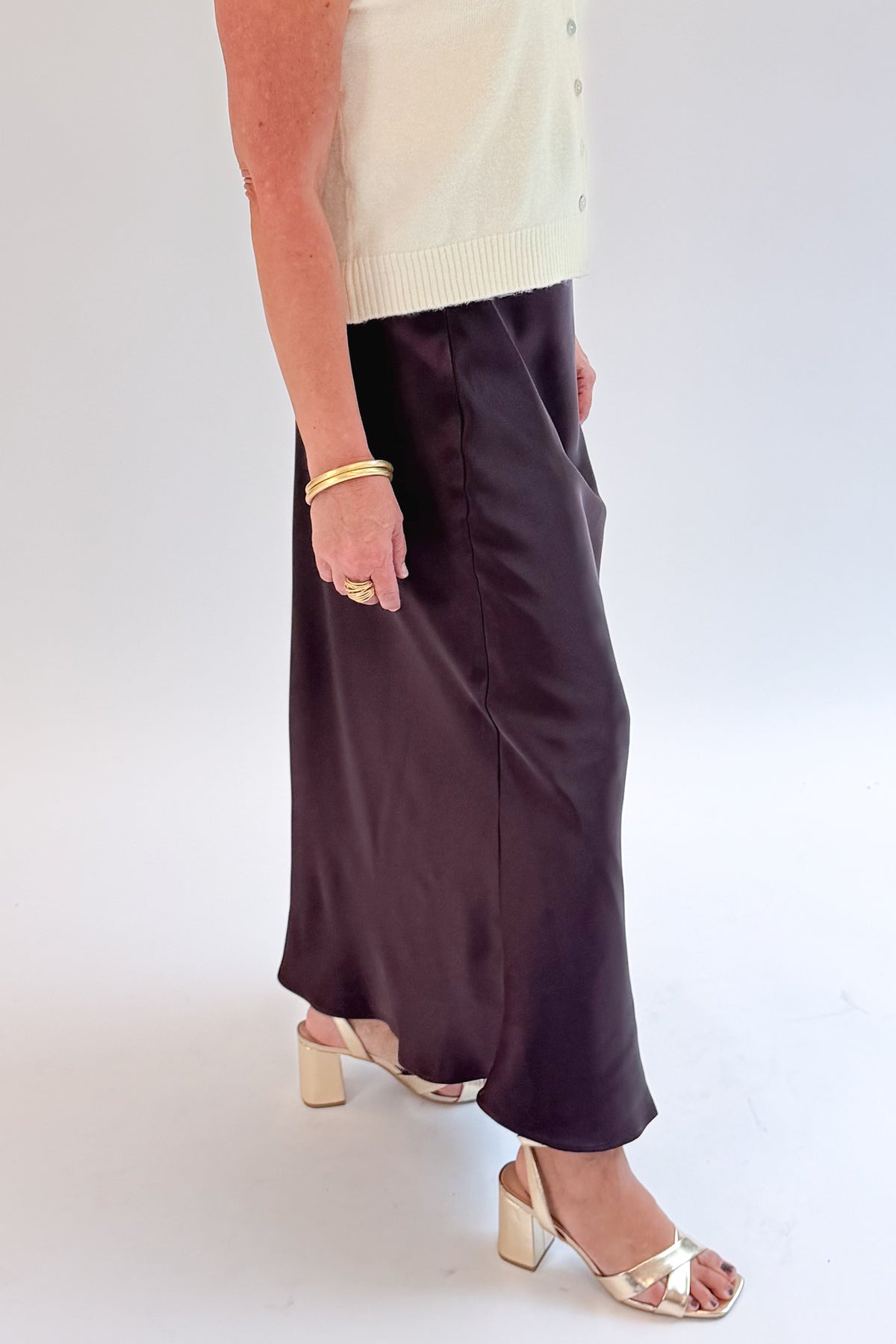 Side detail view of woman wearing Swagger Boutique’s Wine Satin Maxi Skirt with sweater against white studio background.