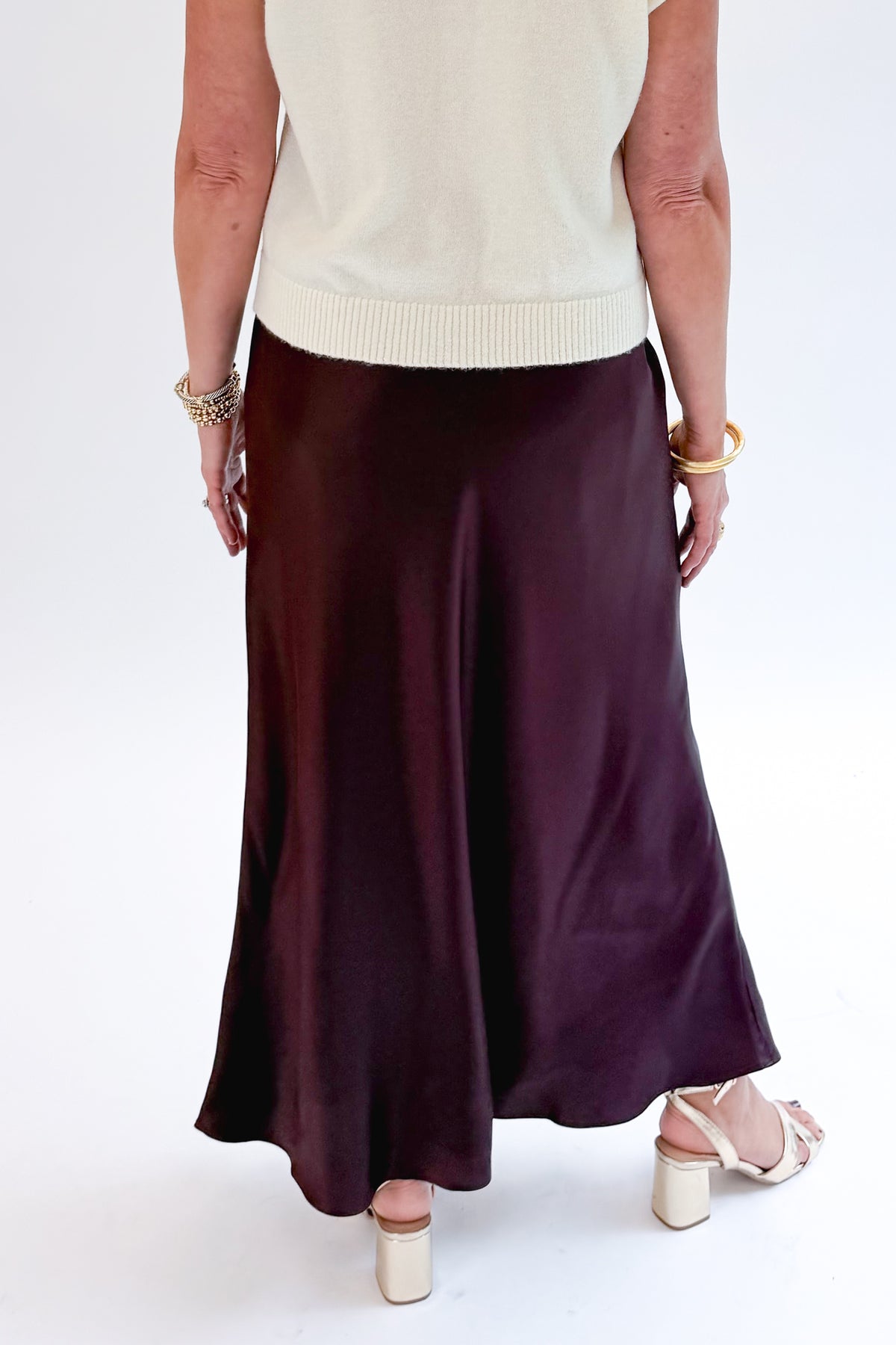 Back detail view of woman wearing Swagger Boutique’s Wine Satin Maxi Skirt with sweater against white studio background.