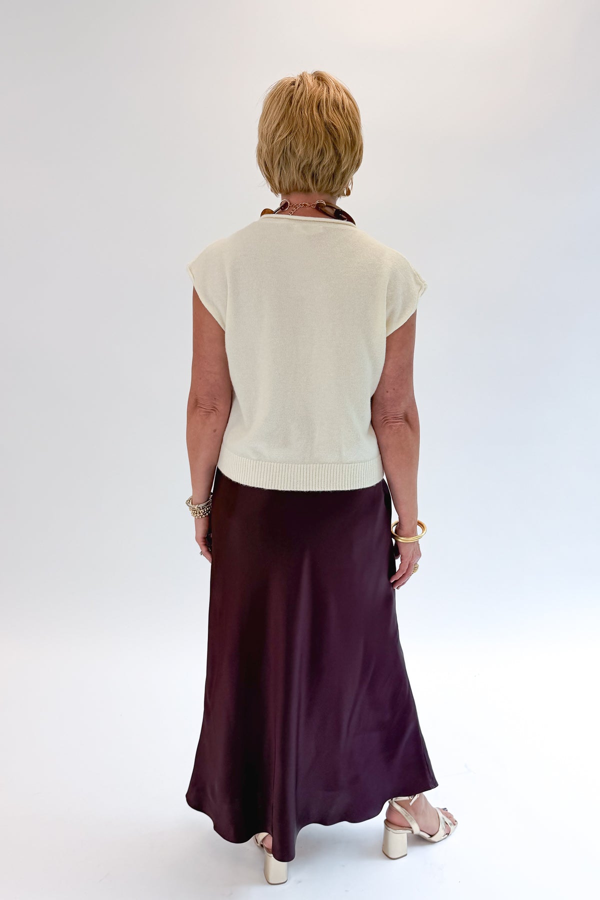 Back view of woman wearing Swagger Boutique’s Wine Satin Maxi Skirt with sweater against white studio background.