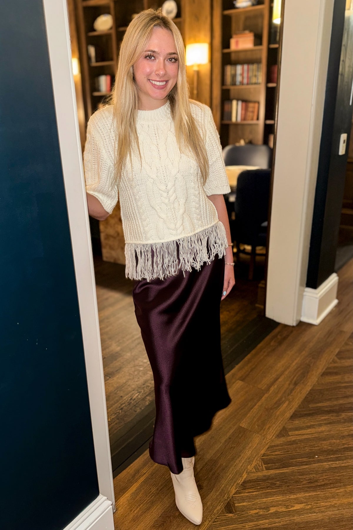Front view of woman wearing Swagger Boutique’s Wine Satin Maxi Skirt with Cream Fringe Short Sleeve Sweater standing outside a den.