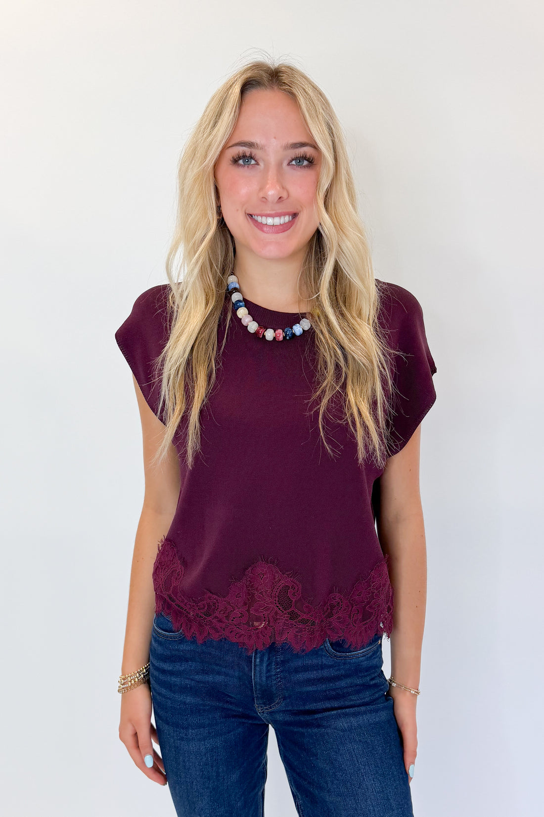 Front view of woman wearing Swagger Boutique’s Wine Short Sleeve Lace Trim Top with jeans against white studio background.