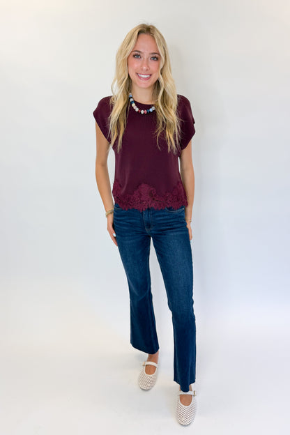 Front view of woman wearing Swagger Boutique’s Wine Short Sleeve Lace Trim Top with jeans against white studio background.