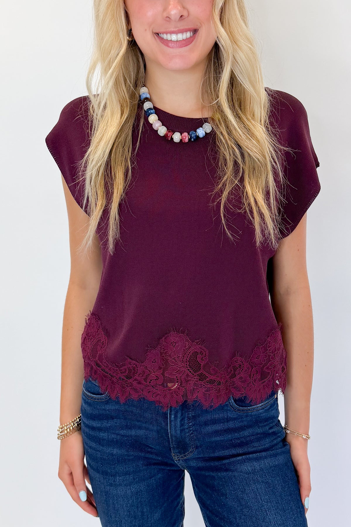 Front detail view of woman wearing Swagger Boutique’s Wine Short Sleeve Lace Trim Top with jeans against white studio background.