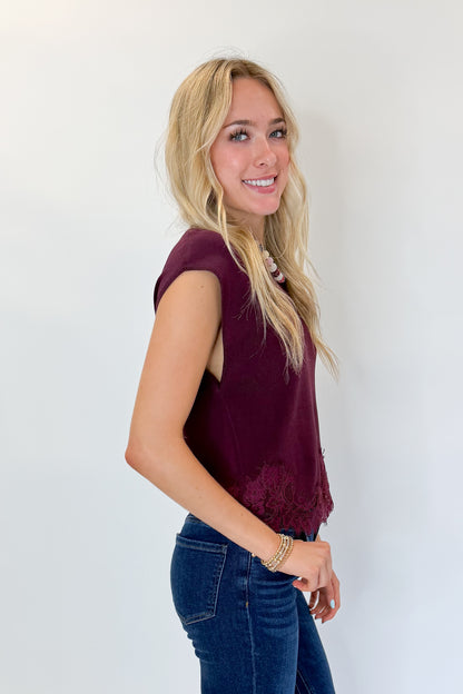 Side view of woman wearing Swagger Boutique’s Wine Short Sleeve Lace Trim Top with jeans against white studio background.
