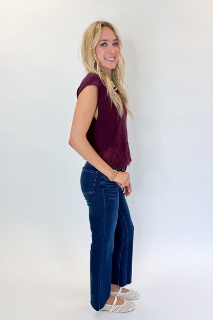 Side view of woman wearing Swagger Boutique’s Wine Short Sleeve Lace Trim Top with jeans against white studio background.