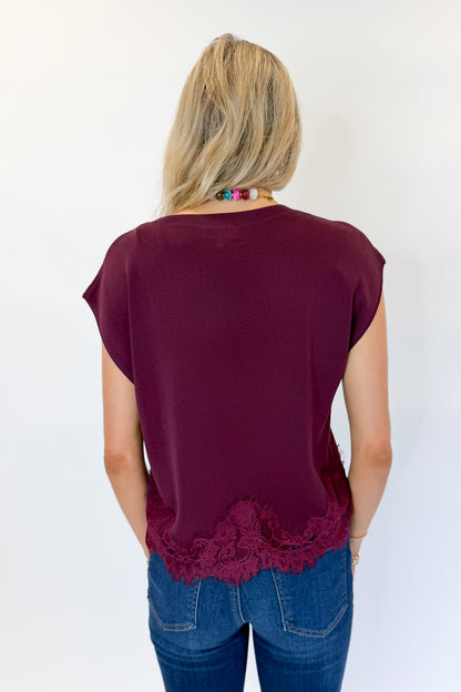 Back view of woman wearing Swagger Boutique’s Wine Short Sleeve Lace Trim Top with jeans against white studio background.