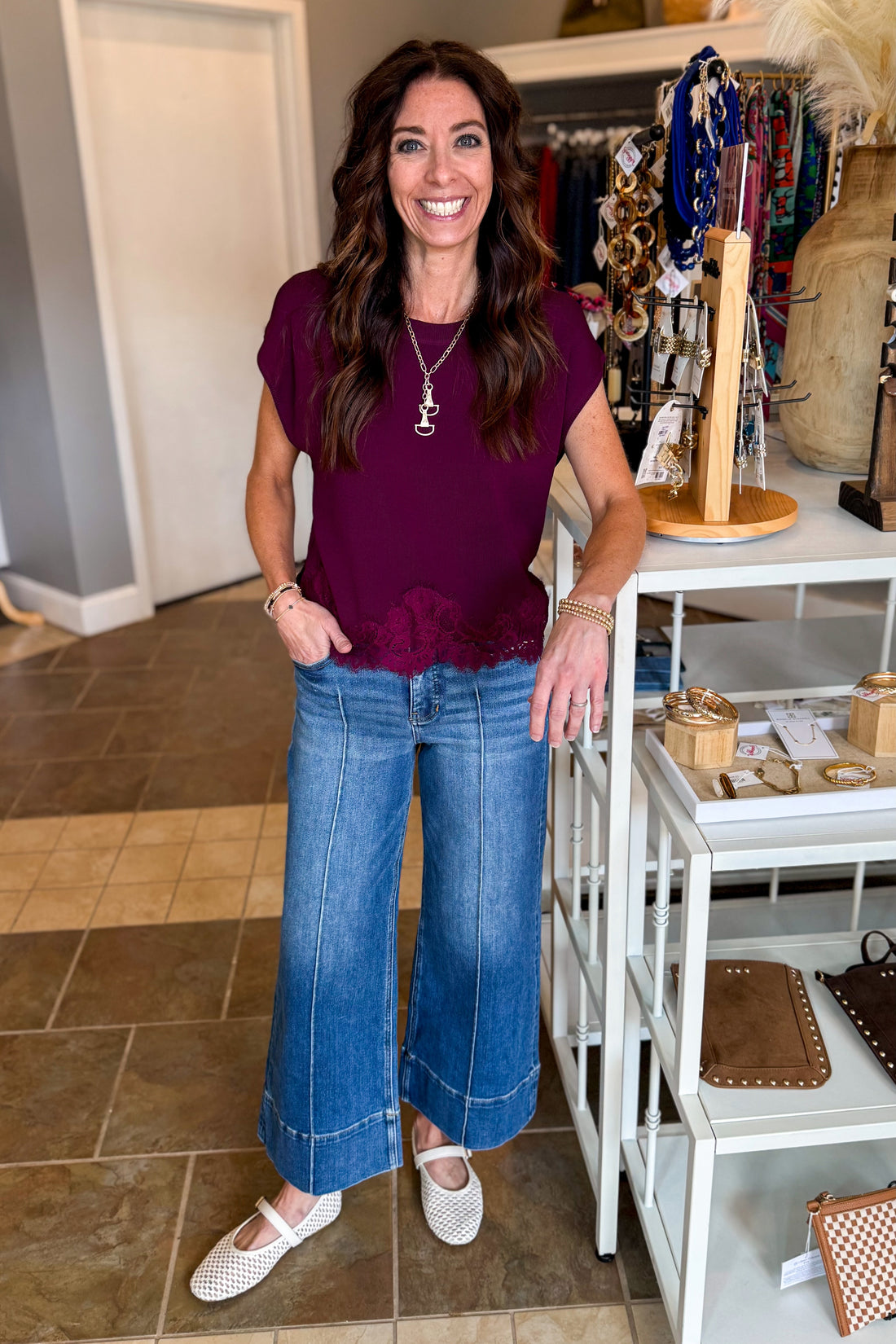 Front view of women wearing Swagger Boutique’s Wine Short Sleeve Lace Trim Top with jeans standing at the store.