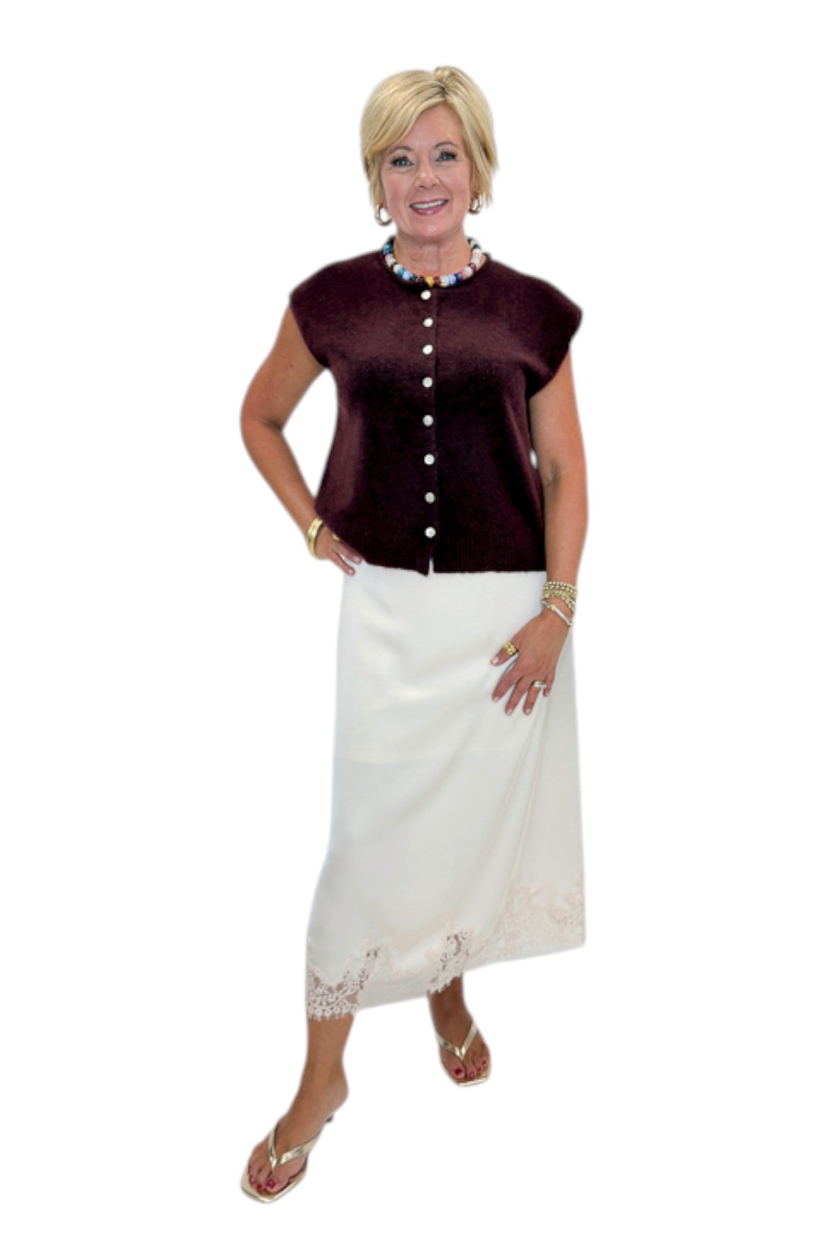 Front view of woman wearing Swagger Boutique’s Wine Sleeveless Button Up Sweater with Ecru Lace Lined Satin Skirt by Entro against white studio background.