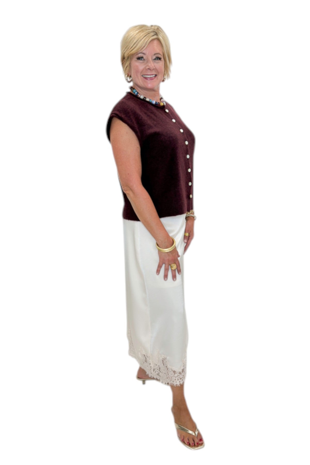 Side view of woman wearing Swagger Boutique’s Wine Sleeveless Button Up Sweater with Ecru Lace Lined Satin Skirt by Entro against white studio background.
