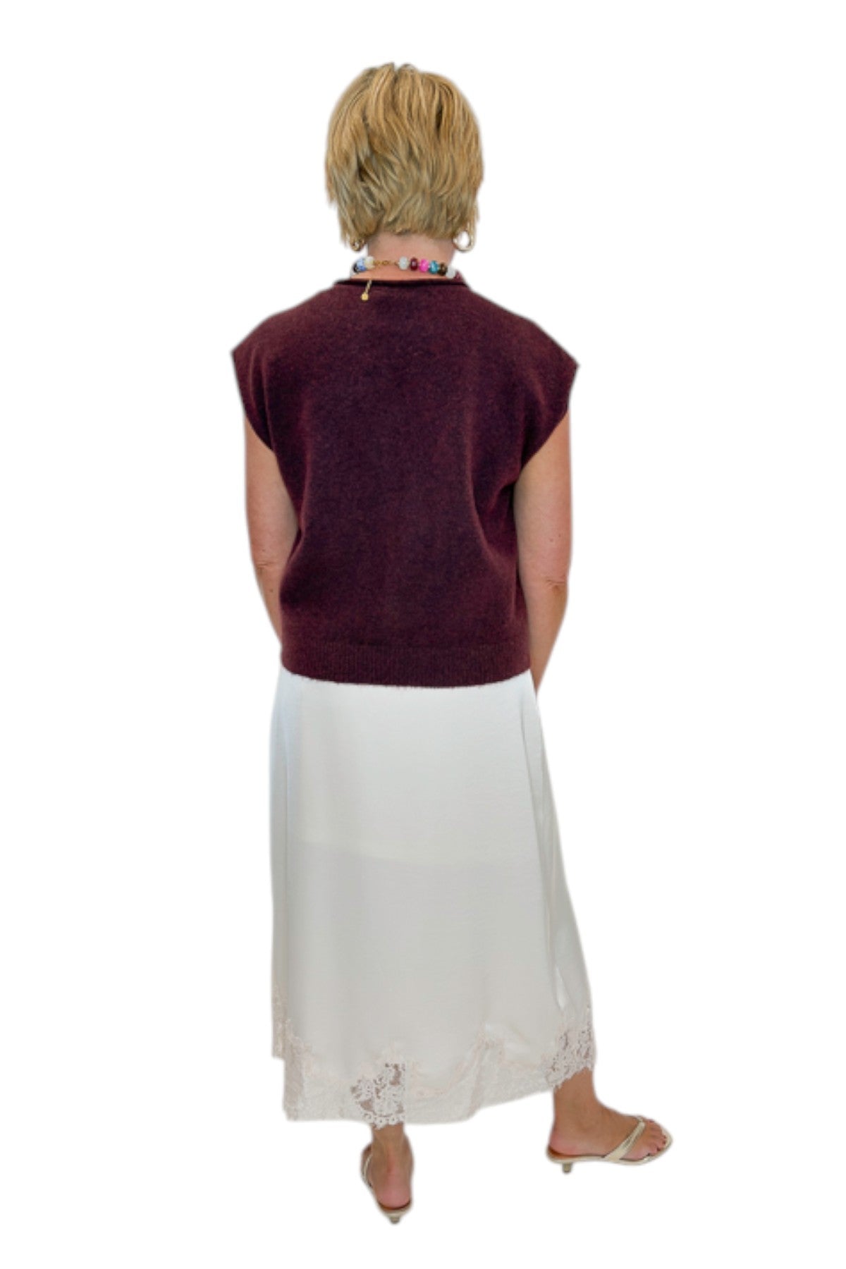 Back view of woman wearing Swagger Boutique’s Wine Sleeveless Button Up Sweater with Ecru Lace Lined Satin Skirt by Entro against white studio background.