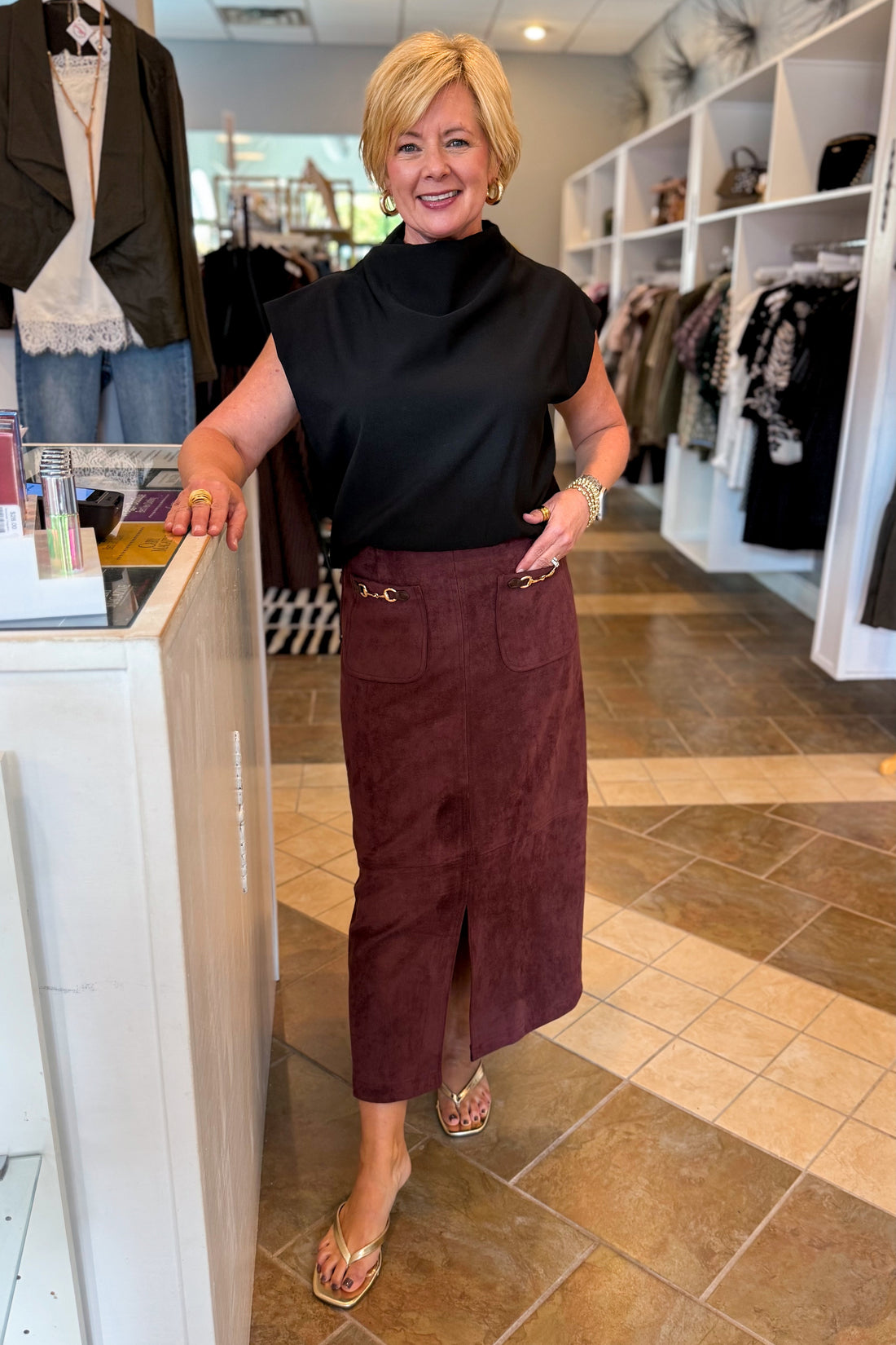 Front view of woman wearing Swagger Boutique’s Merlot Suede Horsebit Pocket Top Skirt by Entro &amp; black sweater standing at the store.