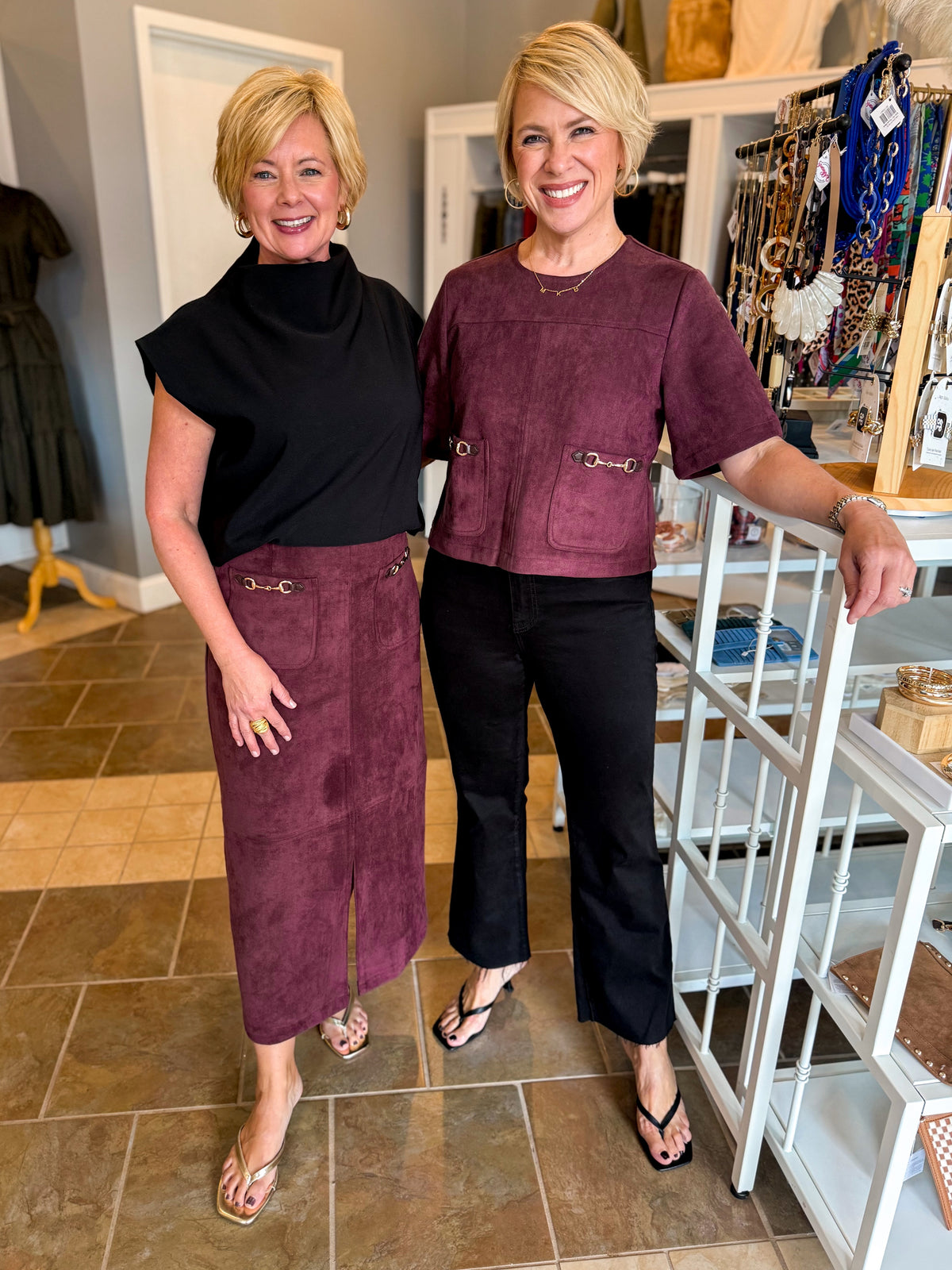Front view of women wearing Swagger Boutique’s Merlot Suede Horsebit Pocket Top Skirt by Entro &amp; black sweater and Merlot Suede Horsebit Pocket Top by Entro with jeans standing at the store together.