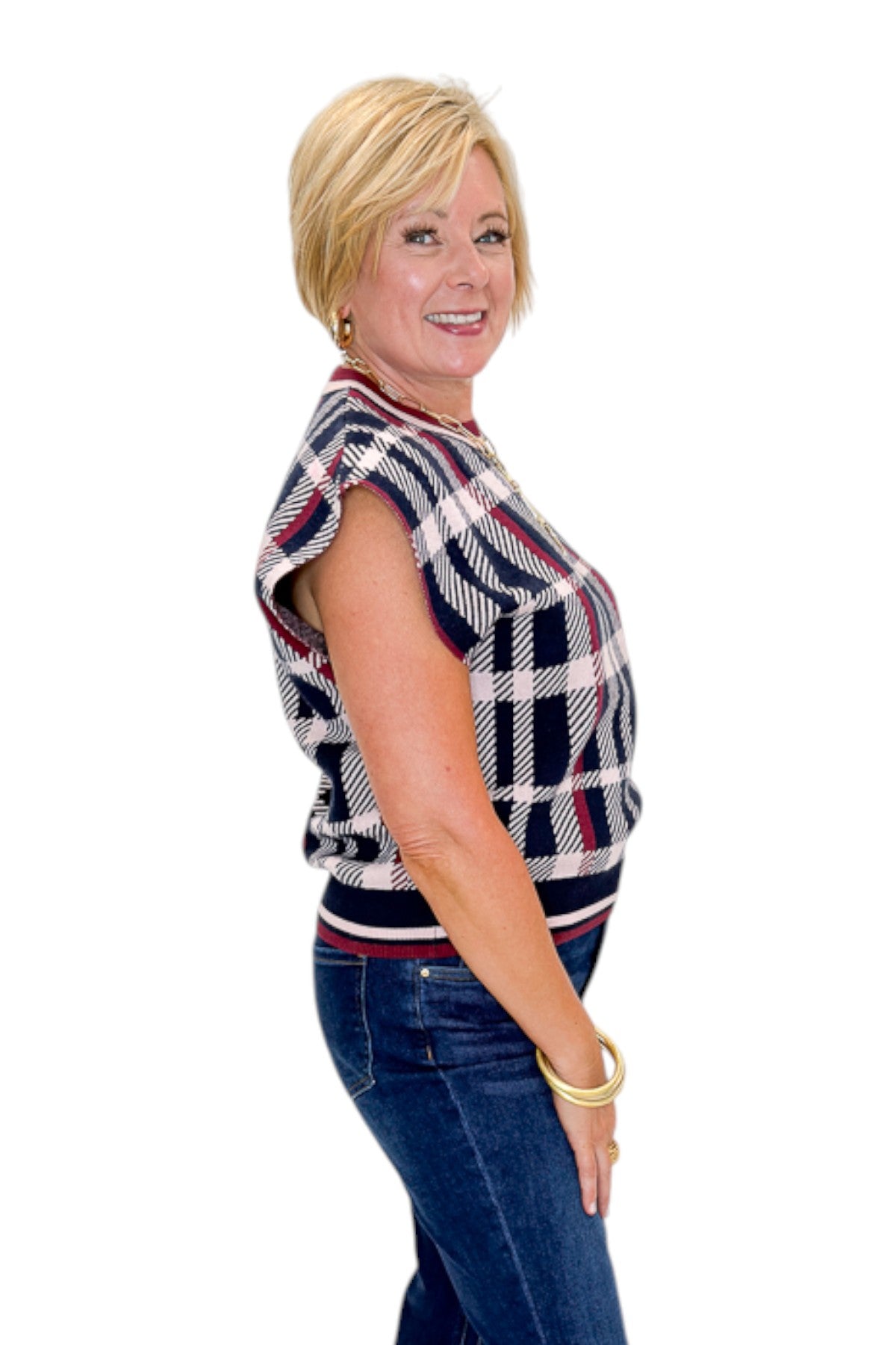 Side view of woman wearing Swagger Boutique’s Wine &amp; Navy Plaid Sleeveless Sweater by THML with jeans against white studio background.