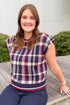 Front view of woman wearing Swagger Boutique’s Wine & Navy Plaid Sleeveless Sweater by THML with jeans sitting on a deck outside.