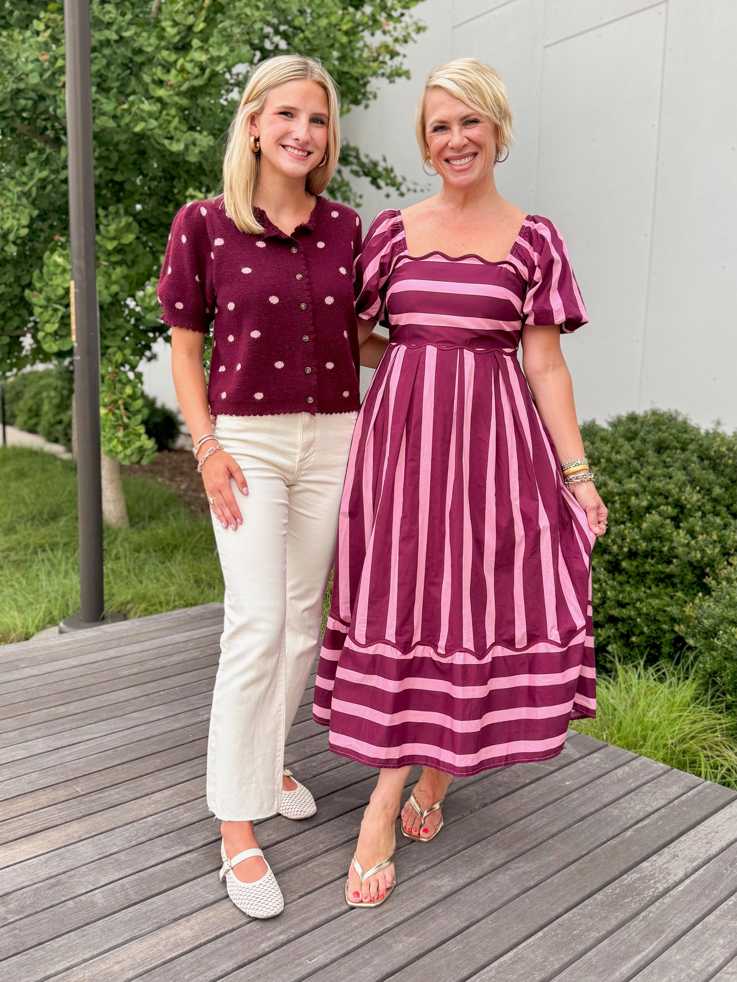 Front view of women wearing Swagger Boutique’s Wine &amp; Pink Polka Dot Short Sleeve Cardigan by Entro with jeans and pink and purple stripe dress standing outside on a deck.