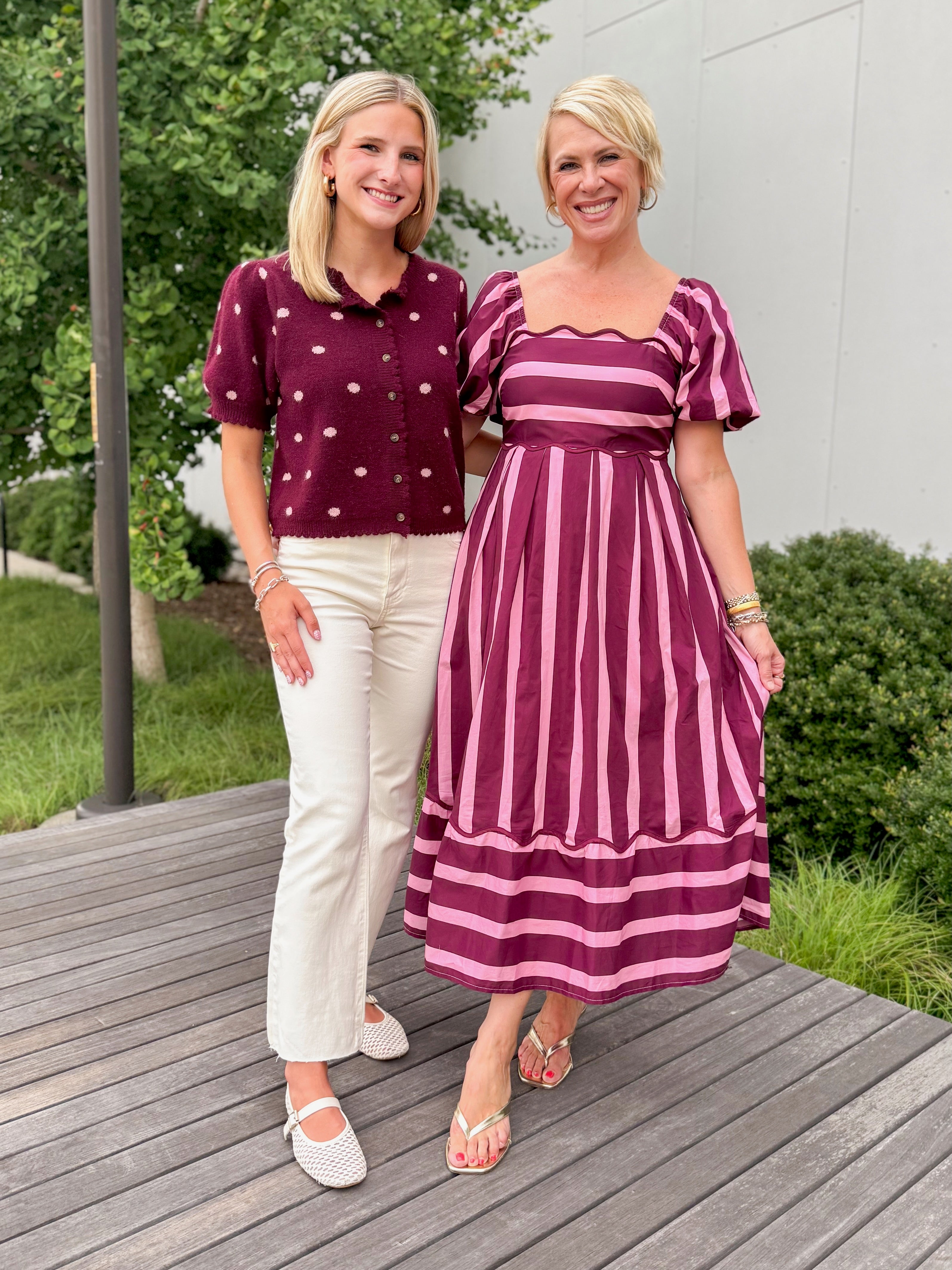 Front view of women wearing Swagger Boutique’s Wine &amp; Pink Polka Dot Short Sleeve Cardigan by Entro with jeans and pink and purple stripe dress standing outside on a deck.