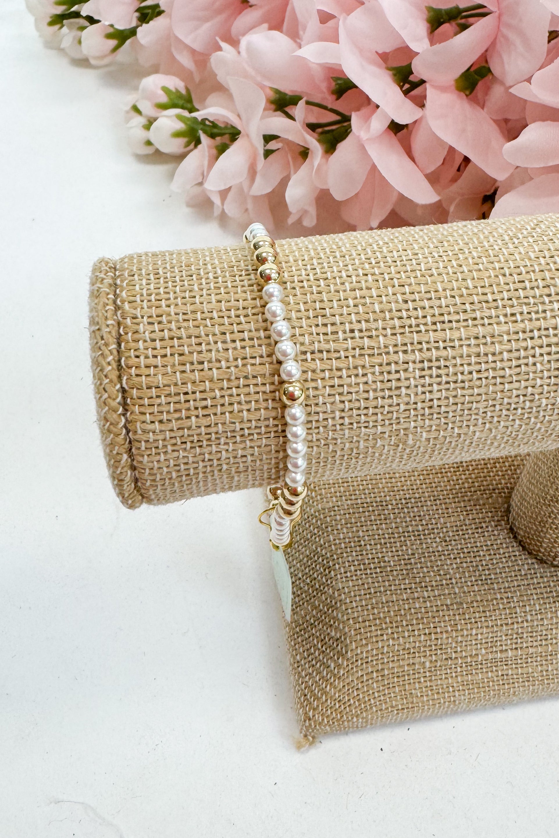 Pearl bracelet on a roll of burlap with pink flowers in the background