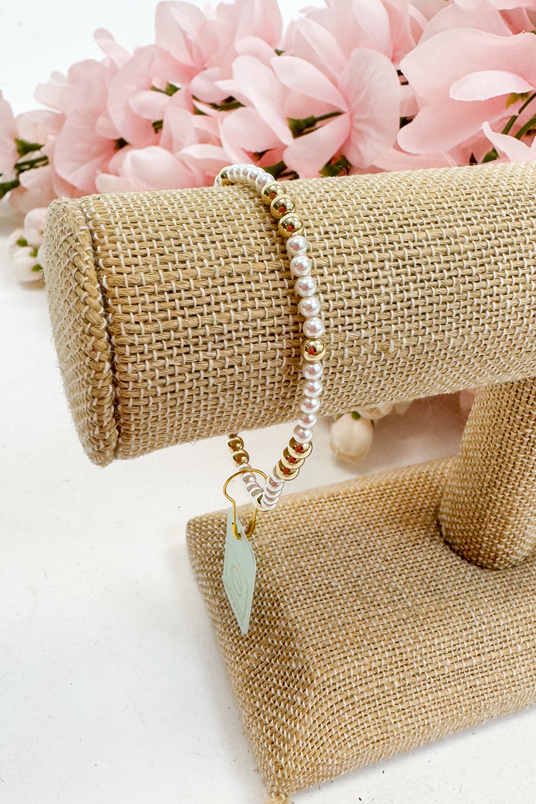 Pearl bracelet with gold accents on a burlap stand with pink flowers in the background