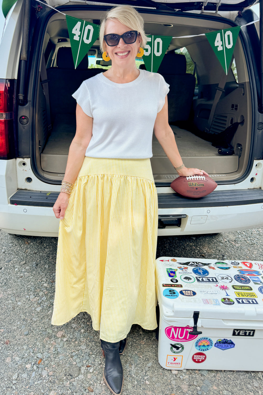 Front view of woman wearing Swagger Boutique’s Yellow Gingham Skirt with white top at a football tailgate.