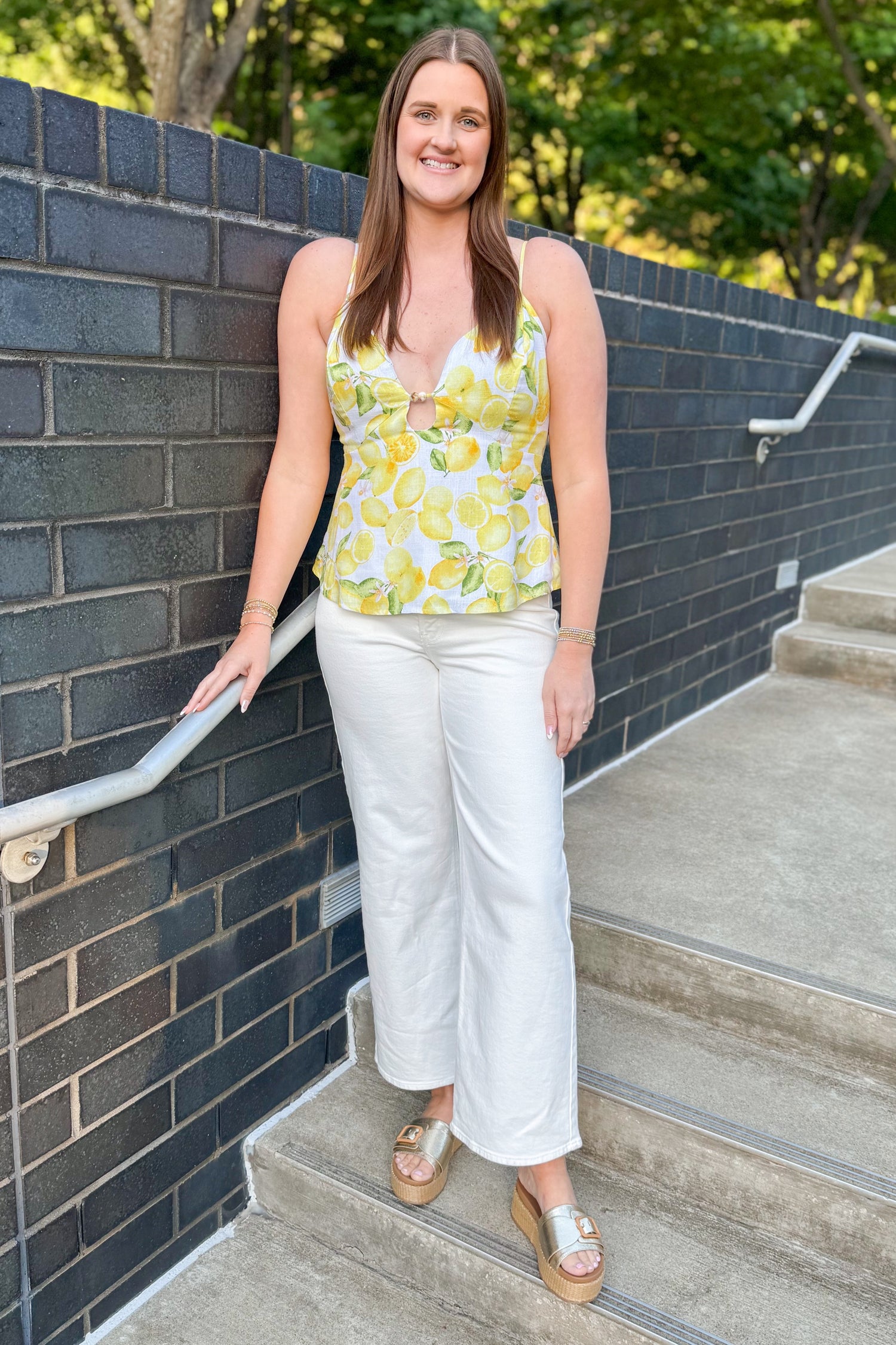 Front view of woman wearing Swagger Boutique’s Yellow Lemon Cut Out Tank with jeans standing outside.
