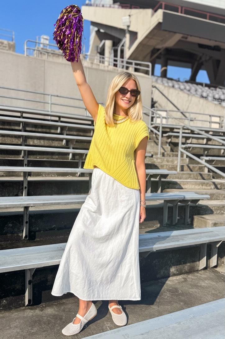 Front view of woman wearing Swagger Boutique’s Yellow Ribbed Detail Sleeveless Sweater by Entro with a skirt at a stadium.
