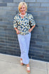 Front view of woman wearing Swagger Boutique’s Yellow & Navy Floral Printed Top with jeans against brick wall outside.