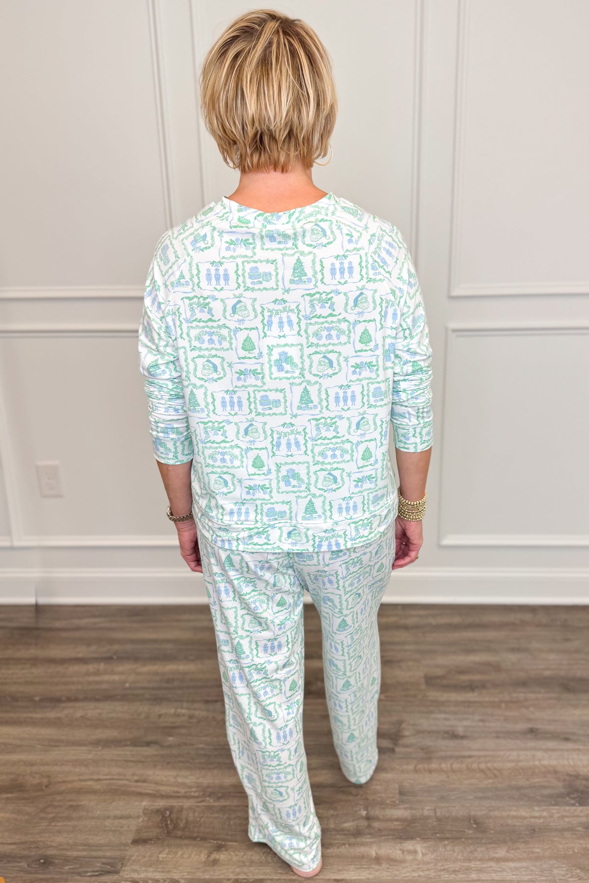Back view of the Yueltide Vignettes Blue Annie Pajama Set, showcasing the allover pastel blue and green Christmas print. The long-sleeve crewneck top features a comfortable, relaxed silhouette paired with matching full-length pajama pants.