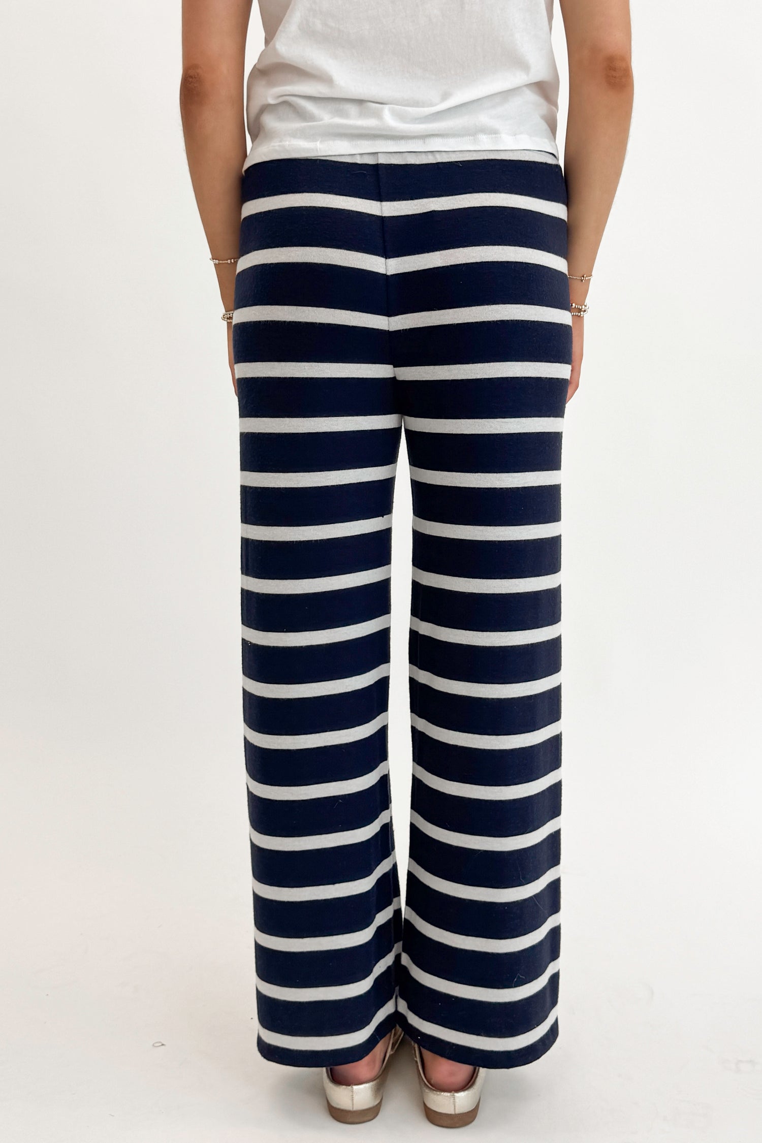 Back detail view of woman wearing Eclipse Overboard Stripe Pant by Z Supply with white top against white studio background.
