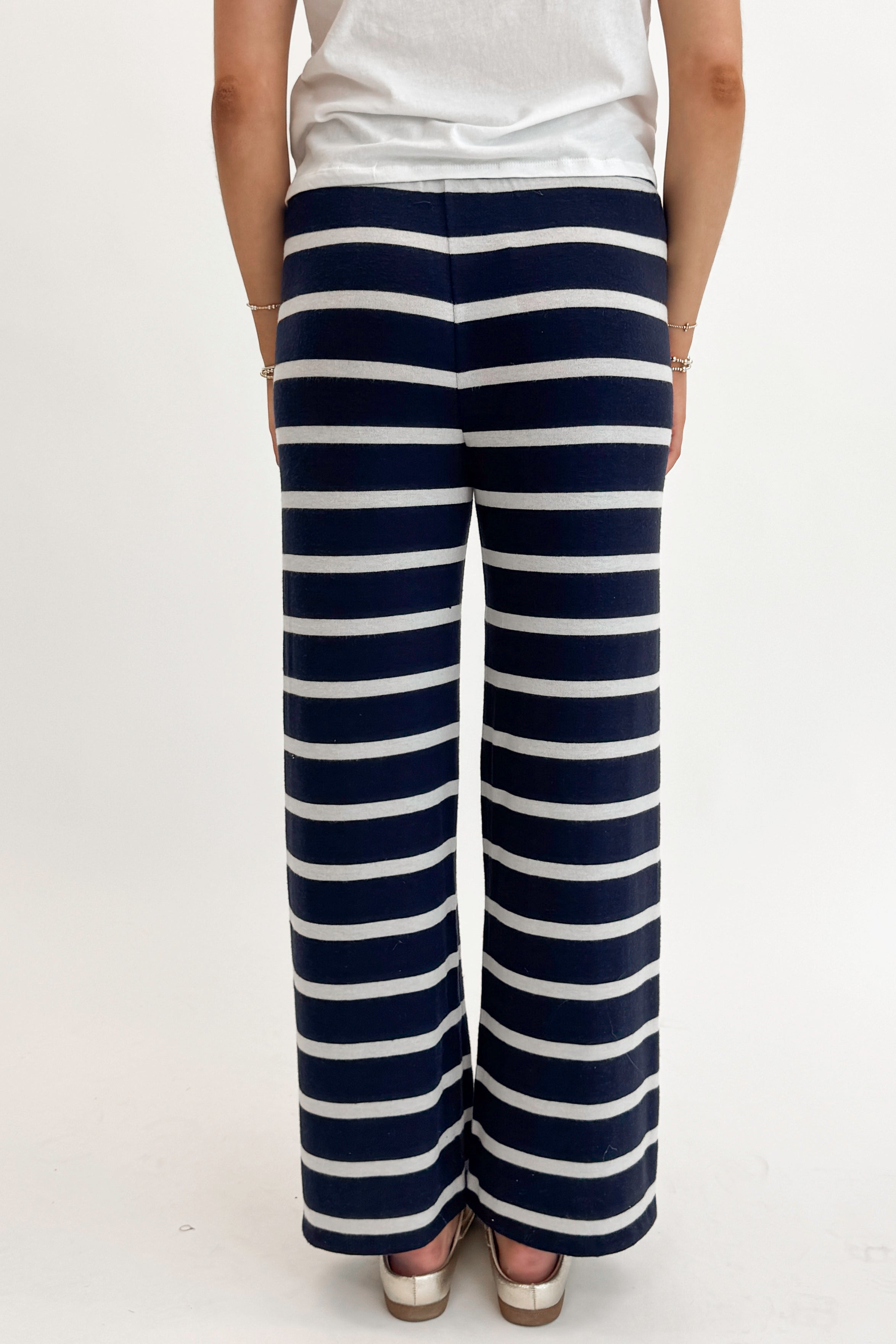 Back detail view of woman wearing Eclipse Overboard Stripe Pant by Z Supply with white top against white studio background.