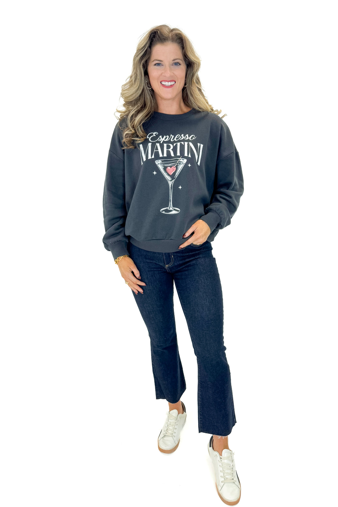 Front view of woman wearing Black Sand Oversized Martini Sweater with jeans against white studio background.