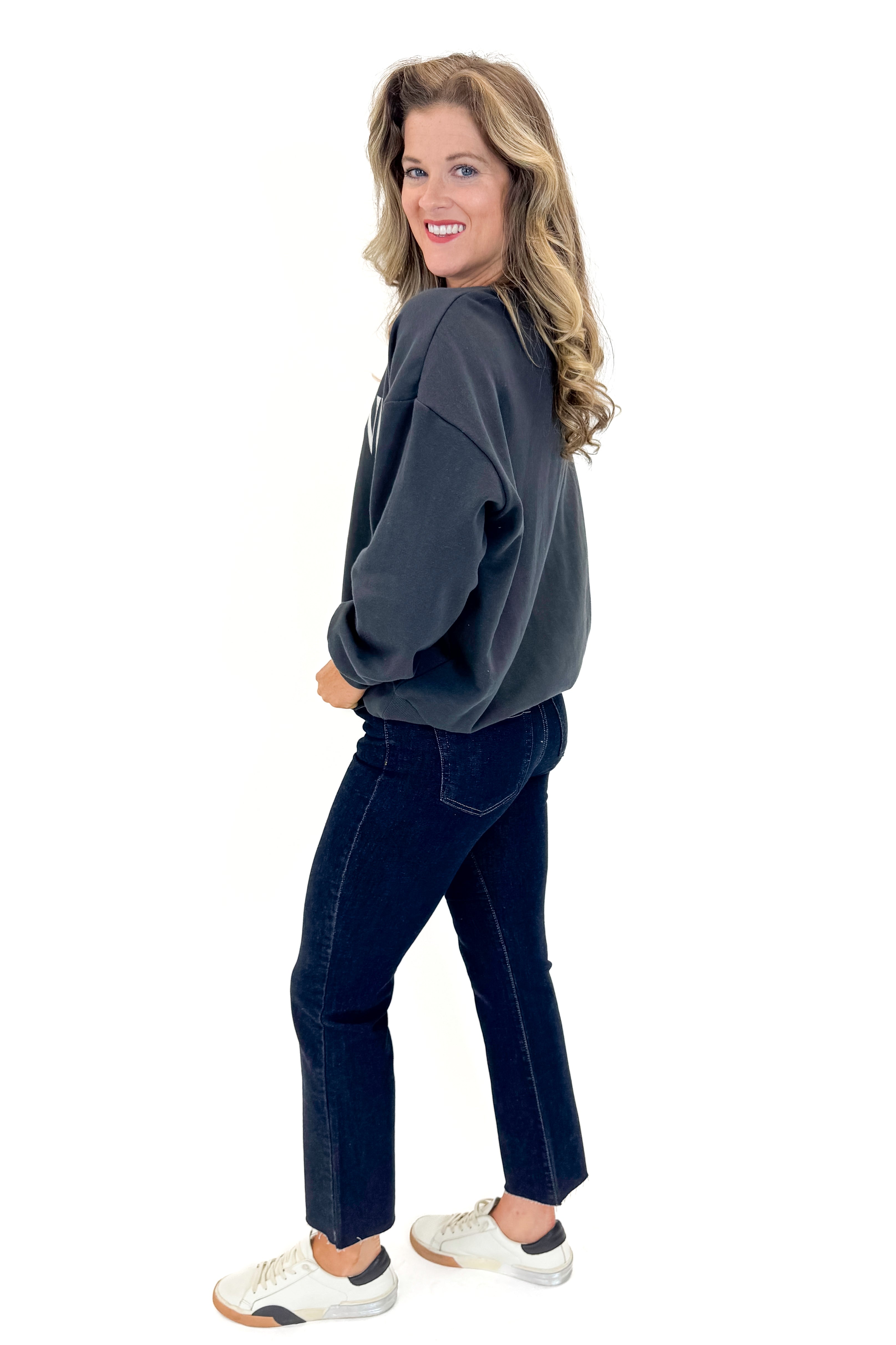 Side view of woman wearing Black Sand Oversized Martini Sweater with jeans against white studio background.