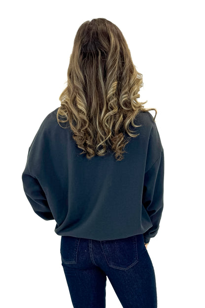 Back view of woman wearing Black Sand Oversized Martini Sweater with jeans against white studio background.