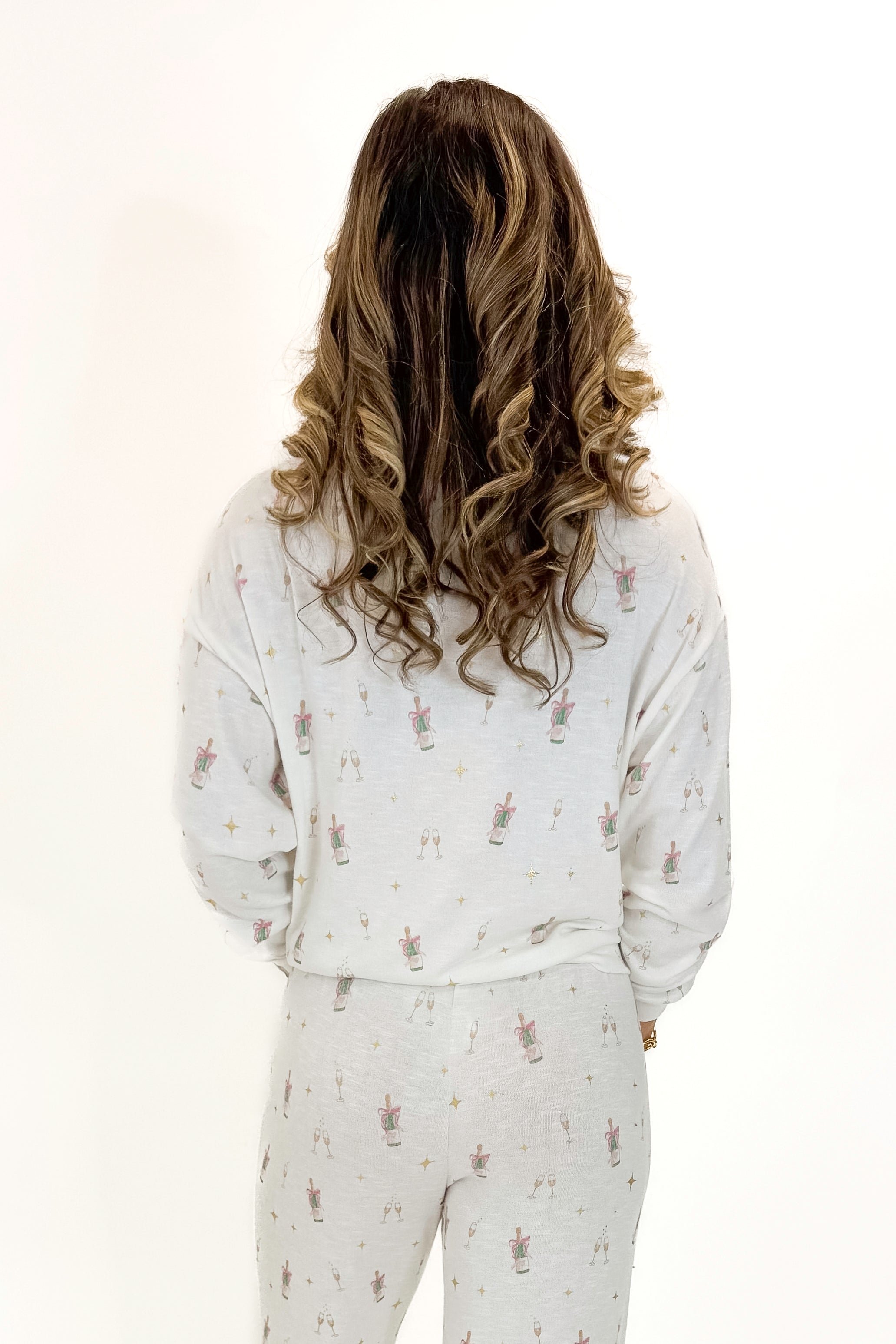 Back view of woman wearing Vanilla Ice Champagne Long Sleeve Top with matching pants against white studio background.