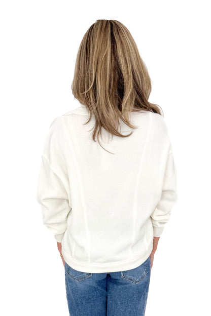 Back view of woman wearing Z Supply cream top with jeans against white studio background.